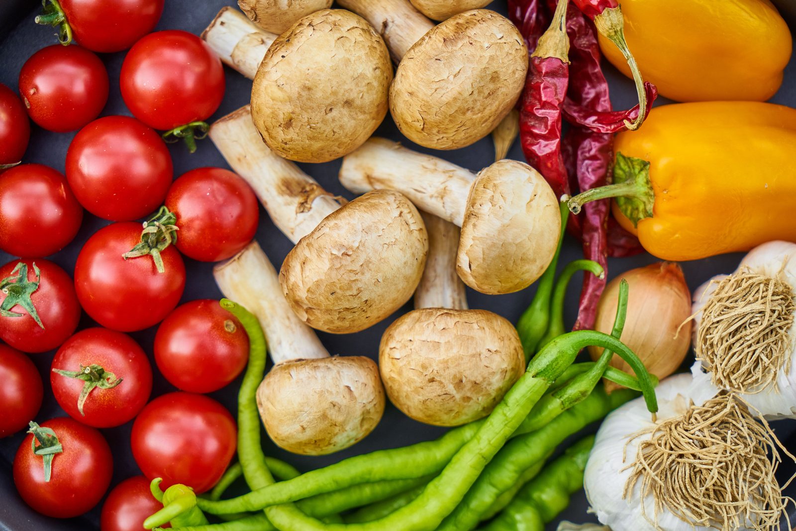 Overhead flat-lay of colorful fresh vegetables including tomatoes, mushrooms, peppers, and garlic