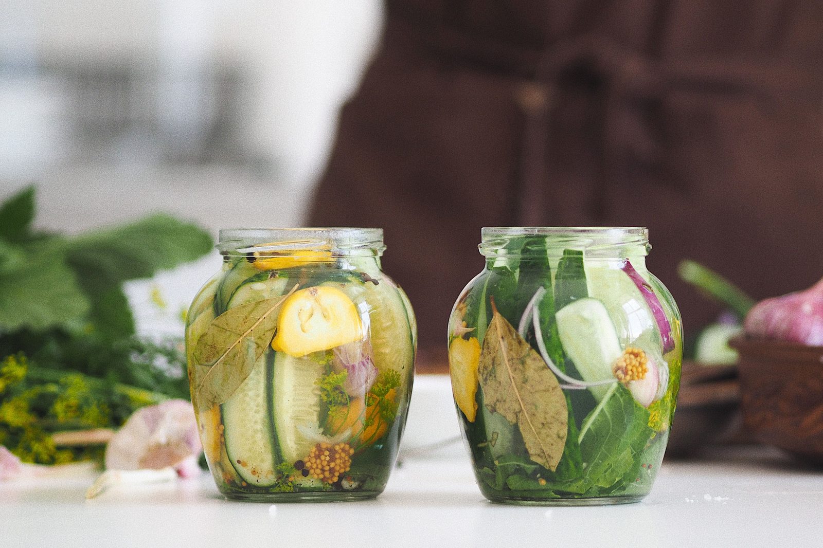Two glass jars of homemade pickled vegetables with fresh herbs on a kitchen counter