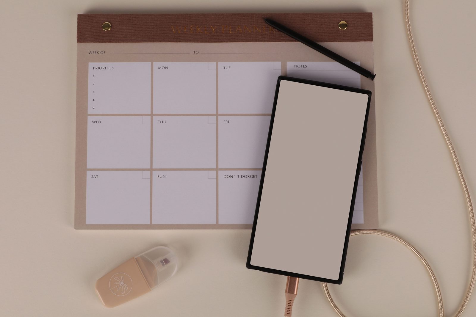 A weekly planner with a priorities and daily grid laid out on a desk, next to a phone and pen
