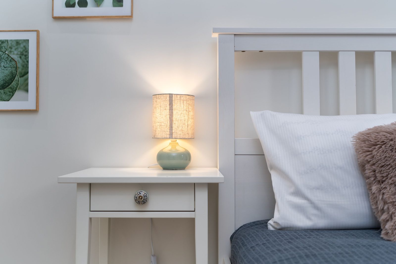 A softly lit lamp on a bedside nightstand next to a bed, set for winding down at night