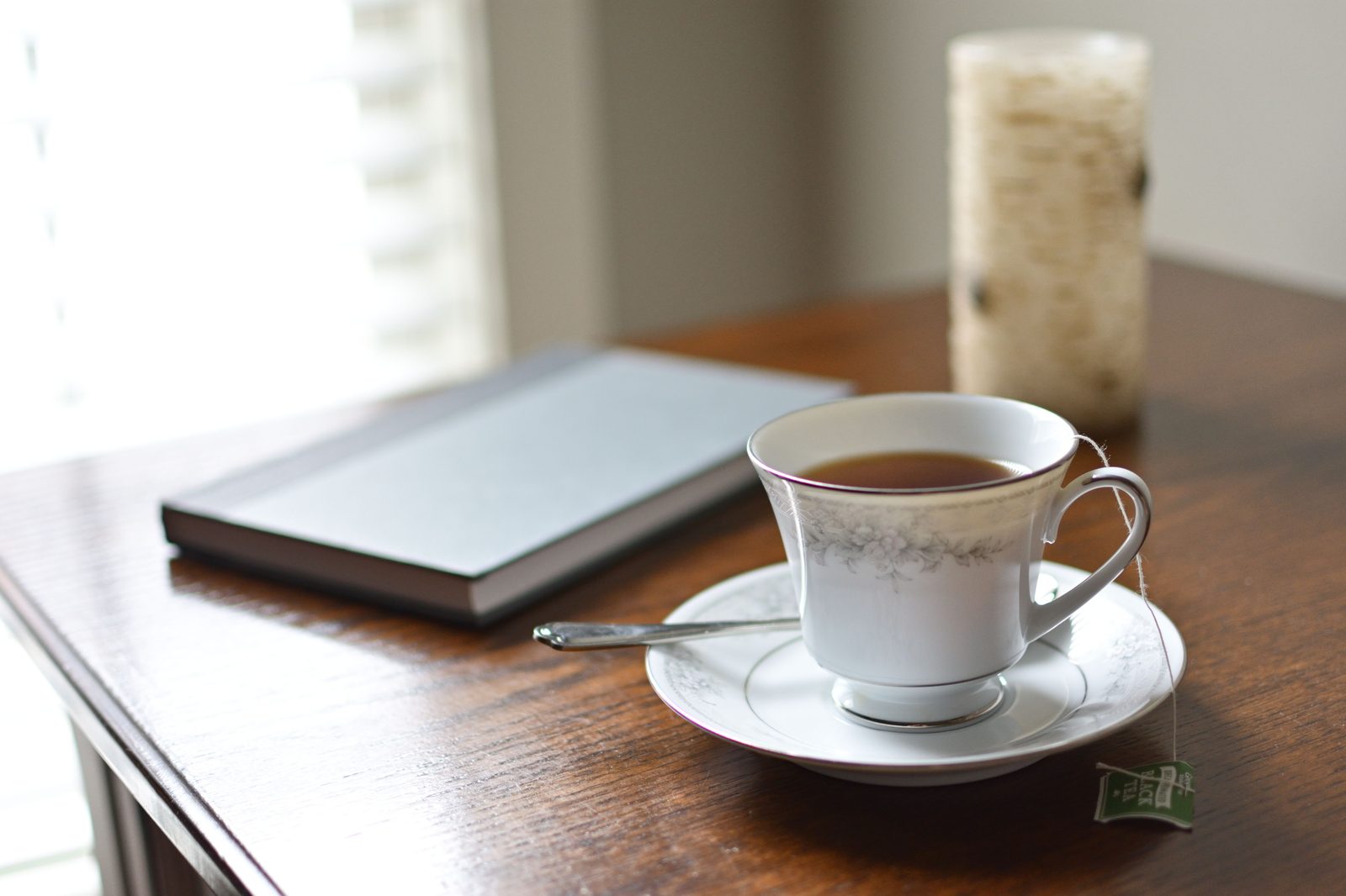 A cup of tea, an open journal, and a candle arranged on a wooden table in warm morning light