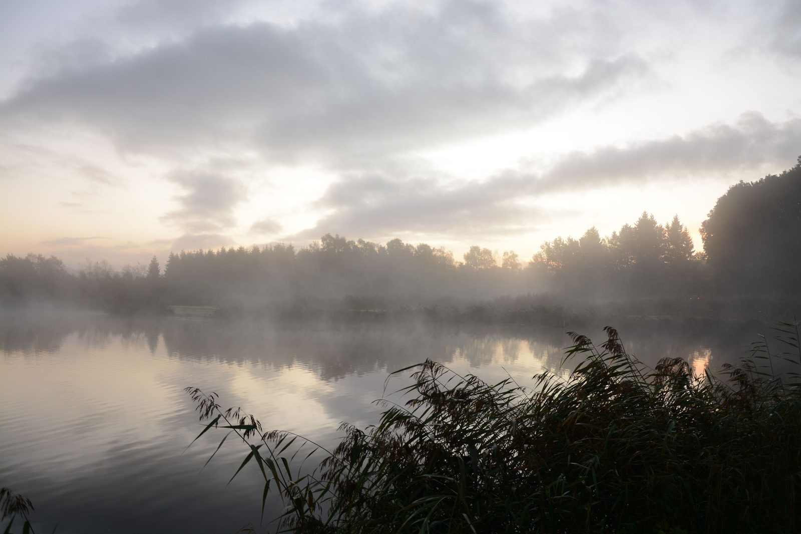 A misty, calm lake at sunrise with still water reflecting the sky